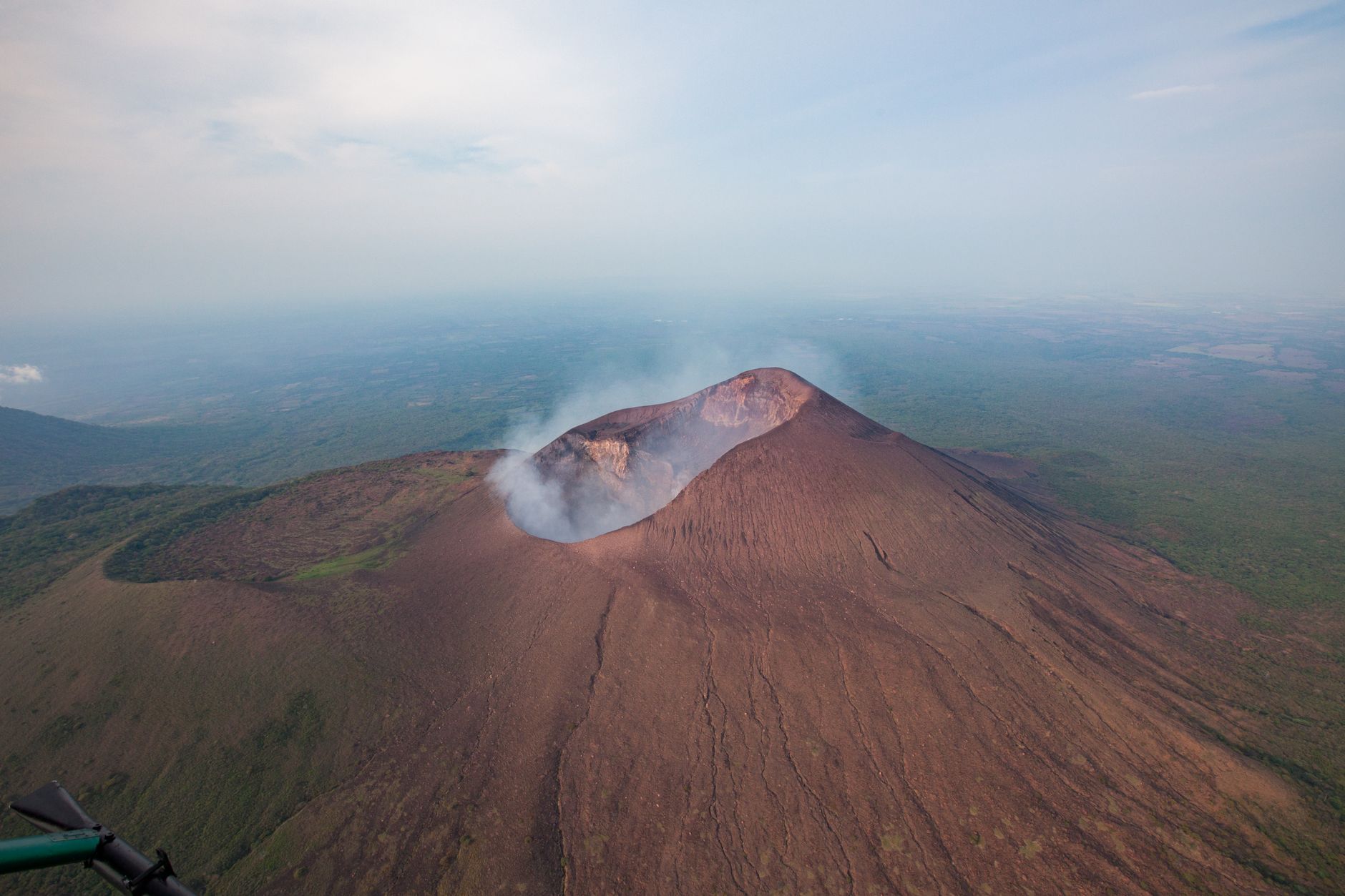 Aerial view of an active volcanic island with visible smoke plume in the Pacific